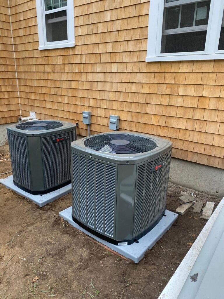 Two Trane outdoor condensers installed side by side on new pads at a cedar shingle home