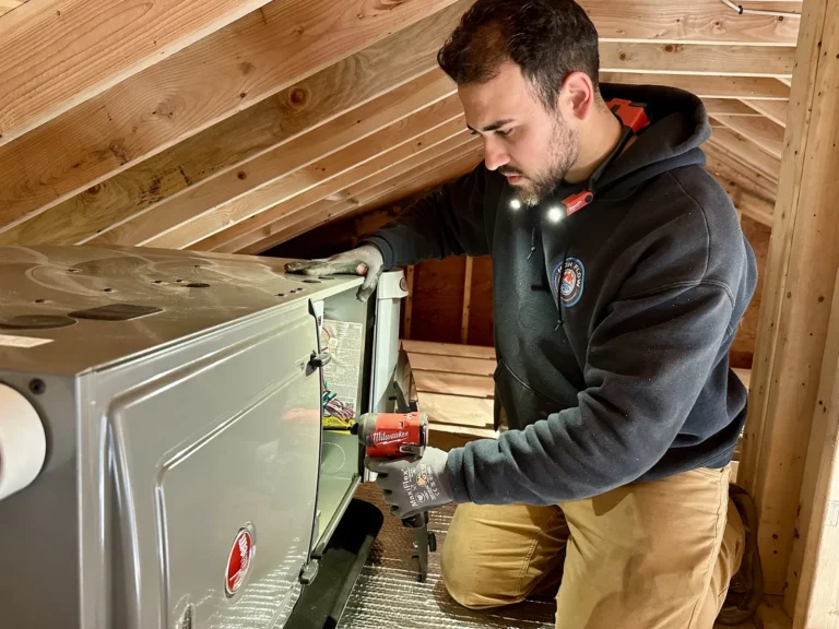High Flow HVAC technician servicing a Rheem gas furnace during a maintenance tune-up in a Cape Cod attic
